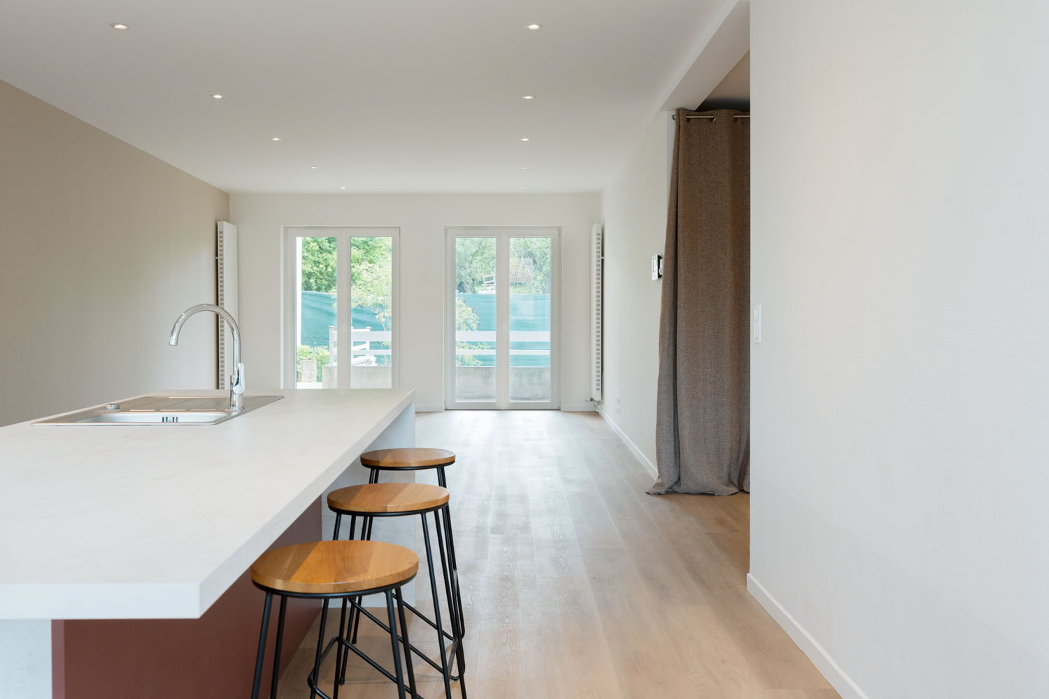 Cuisine ouverte avec îlot central blanc et tabourets en bois, rénovation maison Moselle.