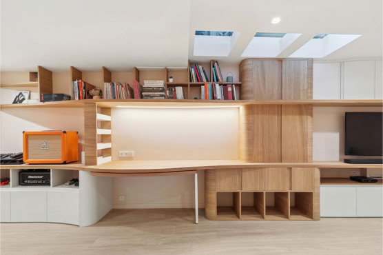 Espace bureau escamotable intégré dans une grande bibliothèque en bois clair avec éclairage LED, par un architecte d’intérieur à Metz.
