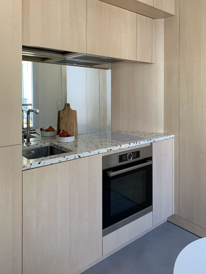 Cuisine minimaliste avec plan de travail en terrazzo et électroménager encastré pour petit appartement.